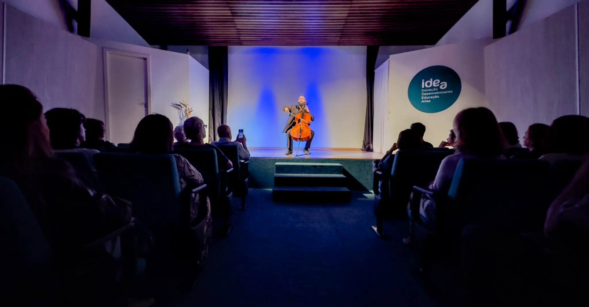 Sala principal do Centro Cultural IDEA em uso, com público e apresentação no palco.